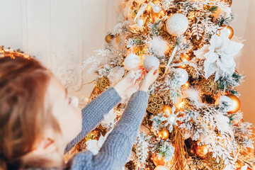 Little girl decorating Christmas tree on Christmas eve at home. Young kid in light bedroom with winter decoration. Happy family at home. Christmas New Year december time for celebration concept.