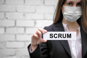 A European girl wearing a medical mask holds a sign with the inscription Scrum, against the...