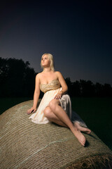 woman sitting on the haystack. portrait of a white girl in nature at night. white girl in the village. young girl enjoys nature
