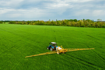 Tractor spray fertilizer on green field in spring drone view, agriculture background concept.