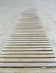 Wooden footbridge in the sand of a beach for access to the sea. Perspective view of beach trotter. Articulated wooden walkway background. Littoral equipment concept.