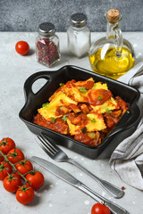 vegan ravioli tomato sauce on black pan on a wooden board. food delivery from restaurant to home.  top view, pasta recipe  Italian cuisine. Takeout coronavirus food. 