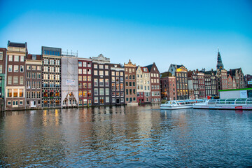 Fototapeta premium AMSTERDAM, THE NETHERLANDS - APRIL 25, 2015: Traditional houses and buildings on the canal with boats on the water