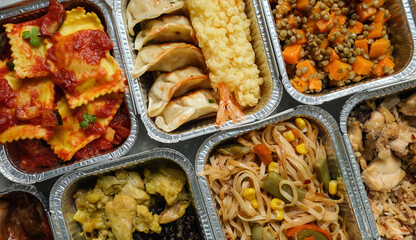Takeout coronavirus food. Different aluminium lunch box with ravioli, curry chicken rice, gyoza tempura, noodles vegetables, lentils with pumpkin. covid-19 takeaway food delivery.	
