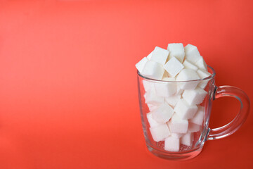 Transparent mug full of refined white sugar cubes on red background. Copy space