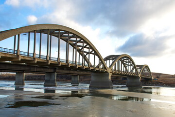 An arched steel and concrete bridge spanning a partially frozen river along the trans-Canada highway in Saskatchewan, Canada.