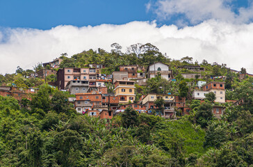 Fototapeta na wymiar Petropolis, Brazil - December 23, 2008: Group of multi-story, red brick cheap housing set on green tropial forested hill under blue cloudscape. Laundry adds color.