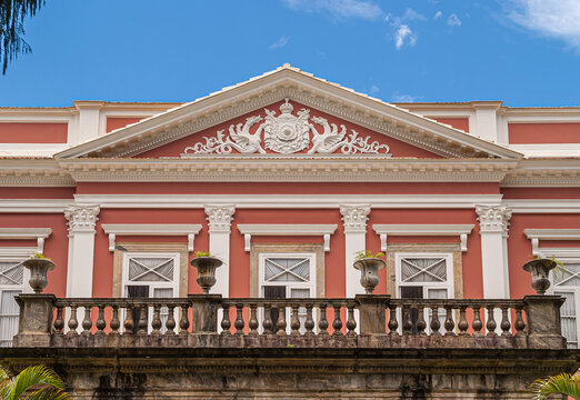 Petropolis, Brazil - December 23, 2008: Imperial emblem in white fresco on pink facade with white frames of windows on Imperial Museu, former palace. Brown molded concrete balcony.