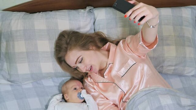 Close up of mother and her newborn baby making video call to father or relatives in a bed. Concept of technology, new generation, family
