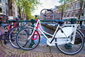 Fototapeta na wymiar AMSTERDAM, THE NETHERLANDS - APRIL 25, 2015: The life of canals and streets. Bikes parked along the bridge
