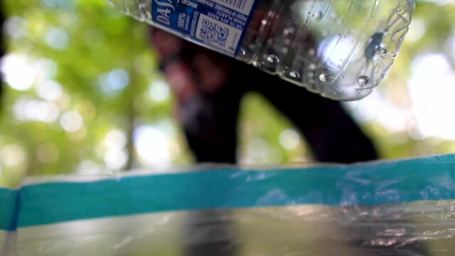 Man Placing Bottle Into Plastic Recycle Bag - Bottle in Focus