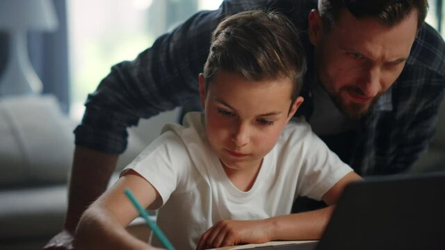 Parent helping child doing homework. Smiling father son looking computer screen.