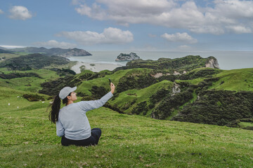 Fototapeta na wymiar Young woman sitting on hillside on Wharariki beach view point. New Zealand