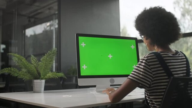 Over The Shoulder Shot Of a Business Woman Working In Office Interior On Pc On Desk, Looking At Display Green Screen. Office Person Using Computer With Computer Green Screen, Sitting at Table.