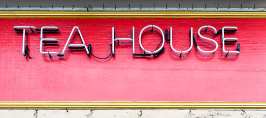 Neon TEA HOUSE sign mounted on red wall with yellow border.