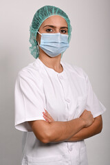 Enfermera posa de lado de brazos cruzados  con una mascarilla quir&uacute;rgica y gorro