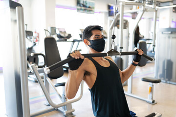 Young man with a mask exercising in the cable machine