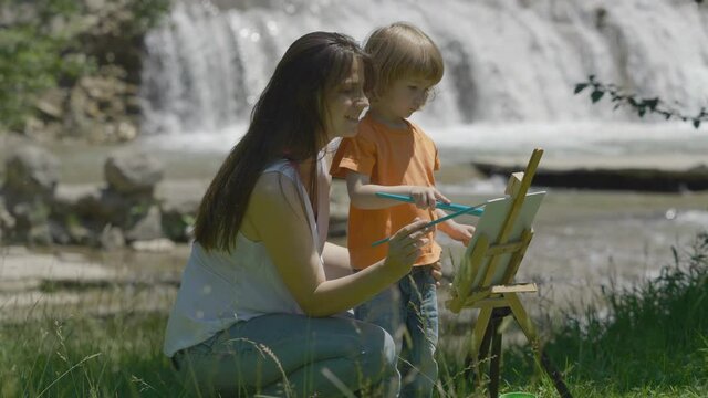 Young mother and little son pain in nature, waterfall flow, free creativity