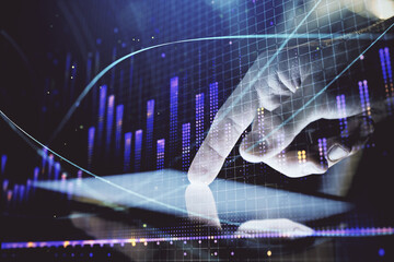 Double exposure of man's hands holding and using a digital device and forex graph drawing. Financial market concept.