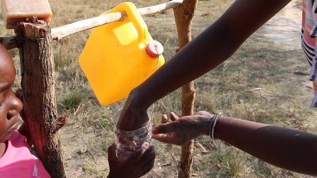 Young girl washing hands on gallon of water recycled and adapted on tree logs as hand washing stations also known as tippy taps, using ash as alternative to soap