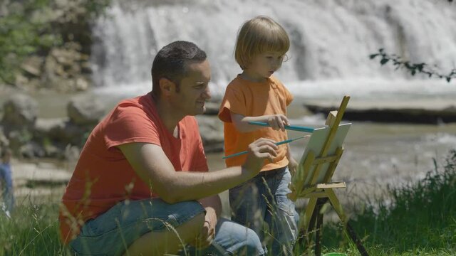 Portrait of father and son painting together in nature, waterfall flow, free creativity, different way to communication between parents and children