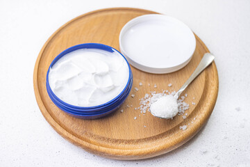 open container with white cream and sea salt in a spoon on a wooden board.