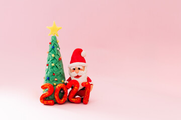 Playful clay christmas concept. Colorful handmade miniature Christmas tree and Santa Claus with mask on pink background. 2021 new year.