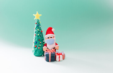 Playful clay christmas concept. Colorful handmade miniature Christmas tree, presents and Santa Claus with mask on green background.