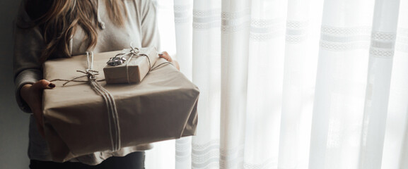 Young woman holds in hands stacked Christmas gift boxes in craft paper with juniper. Christmas presents concept.