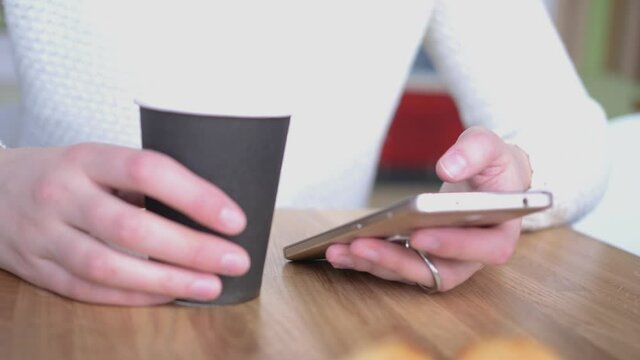 Young woman in cafe works with a smartphone. girl in a cafe uses a tablet and drinks delicious aromatic coffee. woman chatting, drinking coffee and relaxing. close-up.