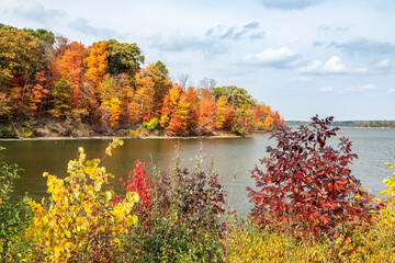 Colorful autumn foliage surrounds the shores of Eagle Creek Reservoir in Indianapolis, Indiana. - obrazy, fototapety, plakaty