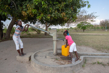 Young girls getting fresh water in the community hand water pump in rural Africa © ivanbruno