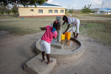 Young girls getting fresh water in the community hand water pump in rural Africa