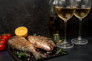 Dinner for two. grilled dorado fish with spices and glasses with white wine on a stone background