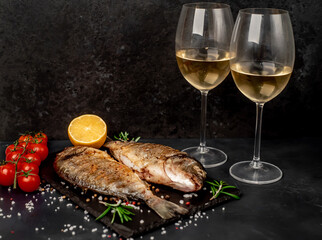 Dinner for two. grilled dorado fish with spices and glasses with white wine on a stone background