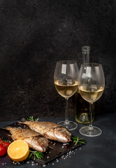 Fototapeta na wymiar Dinner for two. grilled dorado fish with spices and glasses with white wine on a stone background