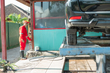 Asian male car cleaner wearing a red uniform and a hat loads the car into the hydraulics at the car wash