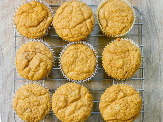 Above view of pumpkin spice muffins arranged on a cooling rack on a brown table. Muffins are a golden color.