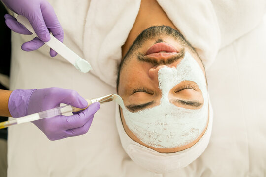 Limpieza facial de un hombre calvo en un spa, con fondo blanco y guantes morados