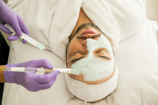 Limpieza facial de un hombre calvo en un spa, con fondo blanco y guantes morados