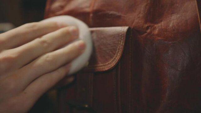 Hand Polishing Flap Of A Brown Leather Bag With Wax - close up