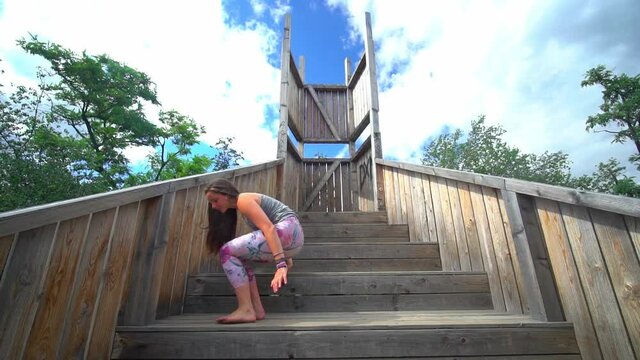 Young woman doing yoga exercise bridge pose outdoors wooden stairs garden, day