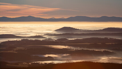 Fototapeta premium Sun light rays during sunshine peaking through morning mist on a wavy landscape.