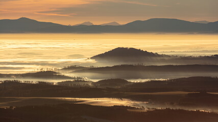 Fototapeta premium Sun light rays during sunshine peaking through morning mist on a wavy landscape.