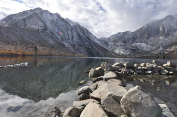 Landscape view of large boulders and  snow capped mountains reflected in the waters at Convict Lake on a cloudy day