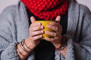 Closeup of a cup of tea in the hands of a woman who covers her neck with a scarf and warms up for the cold winter. Winter concept