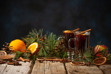 Mulled wine in the glasses with various winter spices on the rustic wooden table on dark blue background decorated with Christmas dried orange and spruce branch. Concept of hot winter alcoholic drink