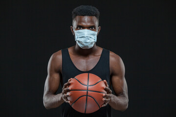 Black male basketball player in protective mask is holding a ball. Preventing the spread of coronavirus infection and pandemics. Healthcare, medicine, sport concept