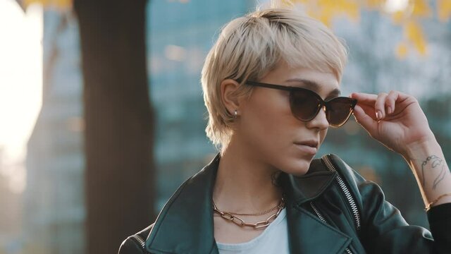 Young woman with bright hair and sunglasses posing in park with hands over the head. Close up. High quality 4k footage