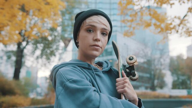 Rebellious teenager, girl, holding the scateboard in the city park in autumn. High quality 4k footage